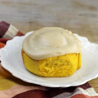 A pumpkin sweet roll on a white round plate.
