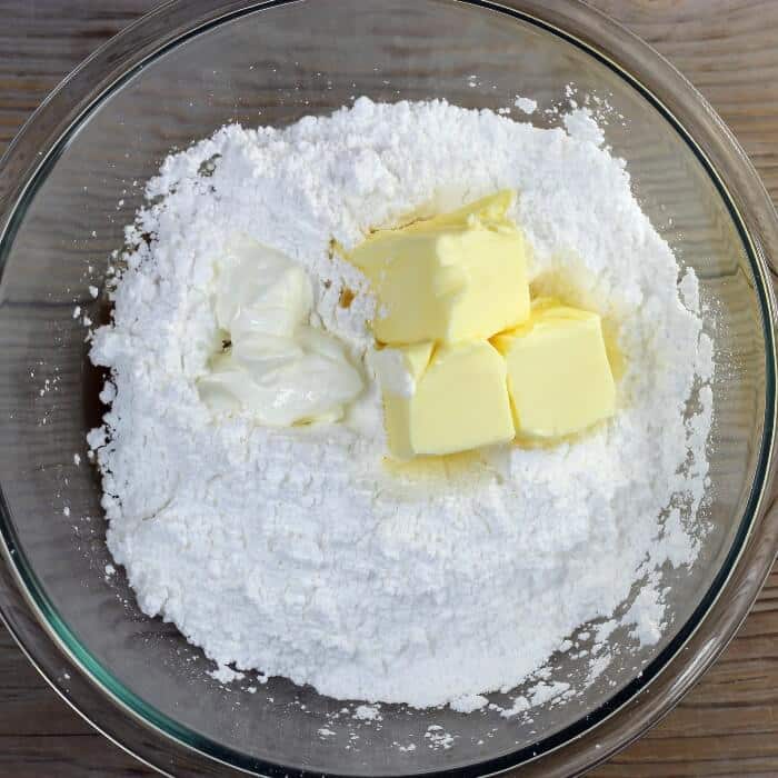 Powdered sugar, butter, sour cream, and vanilla are added to a large bowl.