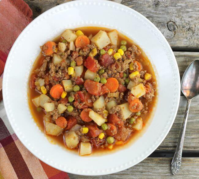 Easy hamburger stew in a white bowl with a napkin on the left side and a spoon on the right side of the bowl.