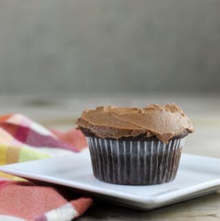 Side view of a chocolate cupcake on a white plate.