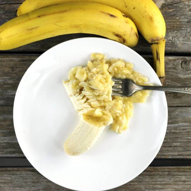 Bananas on the side of a plate with mashed bananas on it.