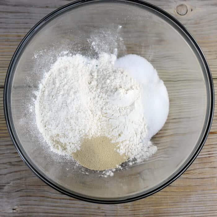 Flour, sugar, salt, and yeast are added to a mixing bowl.