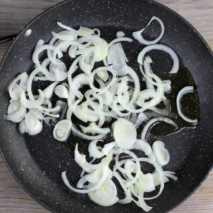 Olive oil and sliced onions are added to a skillet.
