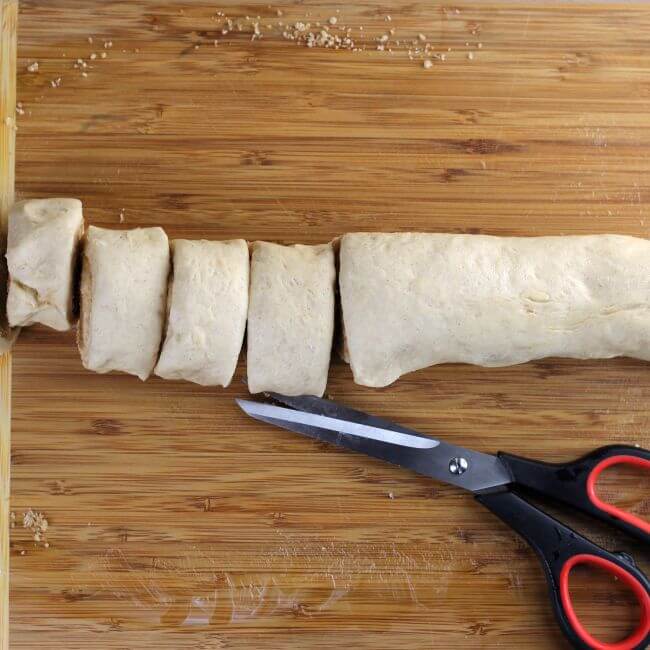 Cutting rolls with a scissors on a cutting board.