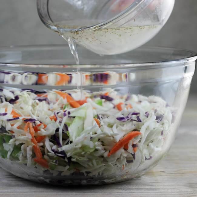 Dressing being poured on the coleslaw mixture.