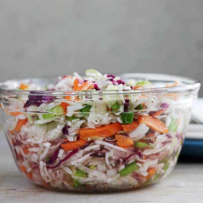 Side view of a bowl of coleslaw with plates to the side. 