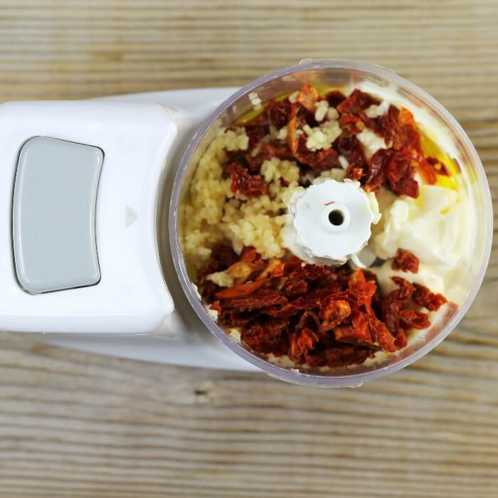 Sun-dried tomatoes, garlic, mayo, lemon juice, and olive oil are added to a mini processor.