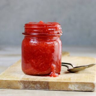 A side view of a jar with strawberry rhubarb sitting on a cutting board.