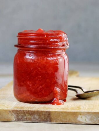 A side view of a jar with strawberry rhubarb sitting on a cutting board.