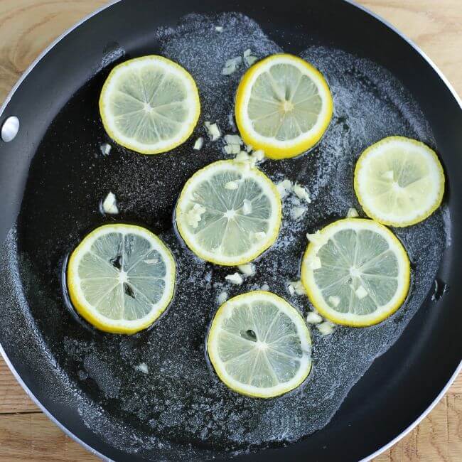 lemon slices and garlic are added to the skillet.