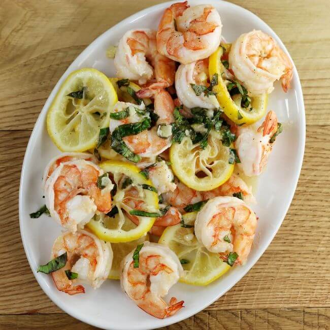 Looking down at a plater of shrimp with lemon slices and basil.