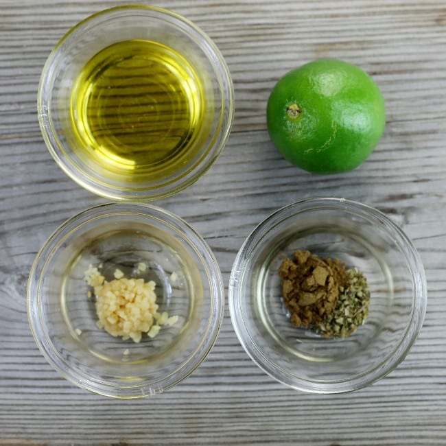 bowls of olive oil, garlic, herbs, and a lime on a table. 