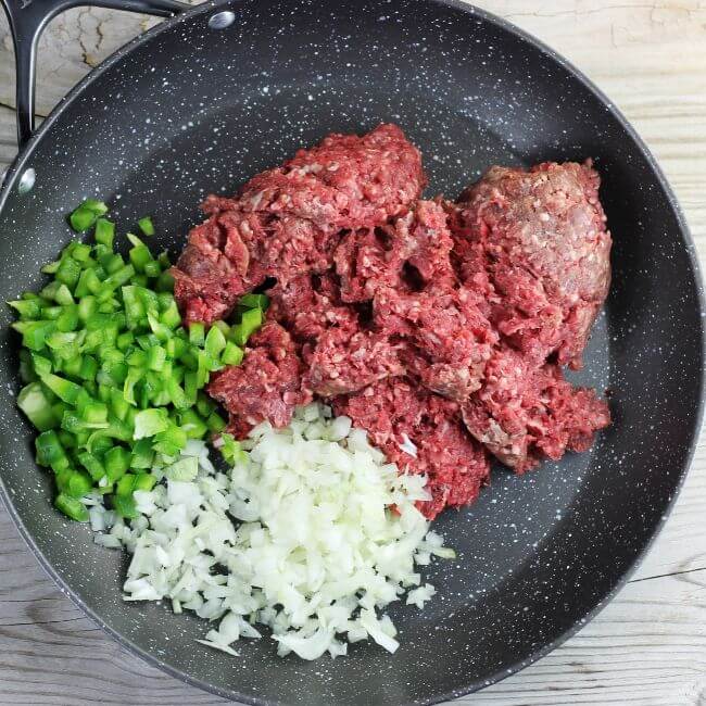 Hamburger, green pepper, and onion are added to a skillet.