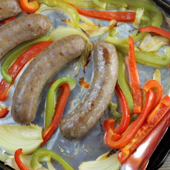 Italian sausage baking in a baking pan with peppers and onions.