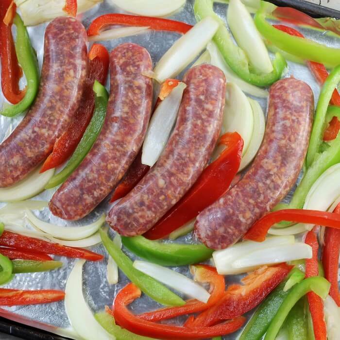 Raw sausage with peppers and onion are arranged on the baking pan.