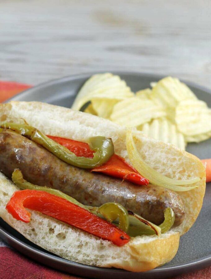 A side angle view of an Italian sausage in a bun with peppers and onion.