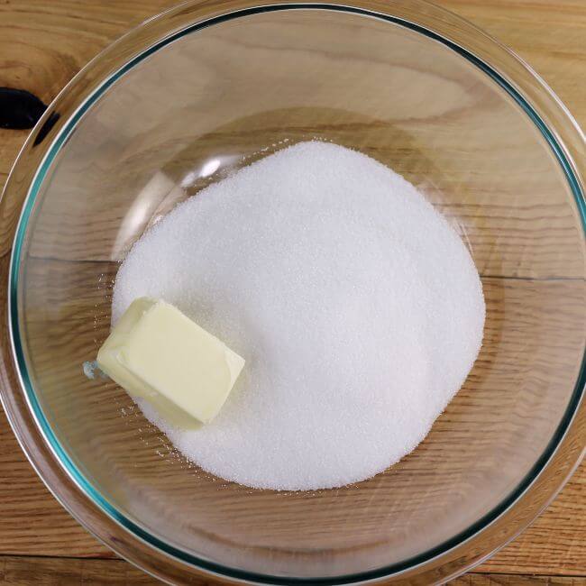 Butter and sugar are added to a glass mixing bowl.