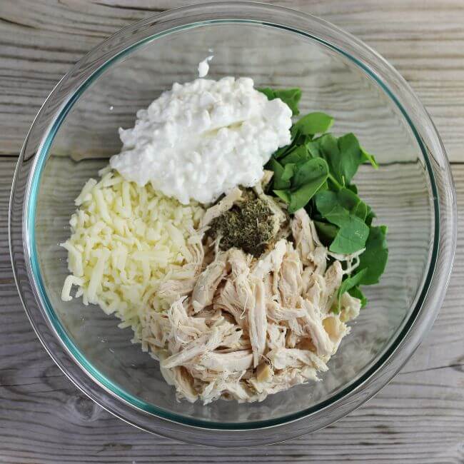 Cheese, shredded chicken, spinach, cottage cheese in a glass bowl.