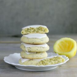 A large stack of cookies on a white plate with a lemon rind in the back.