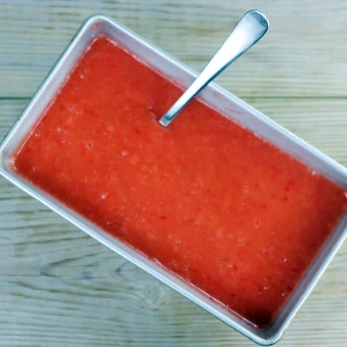 Strawberry sorbet in a loaf pan with a spoon.