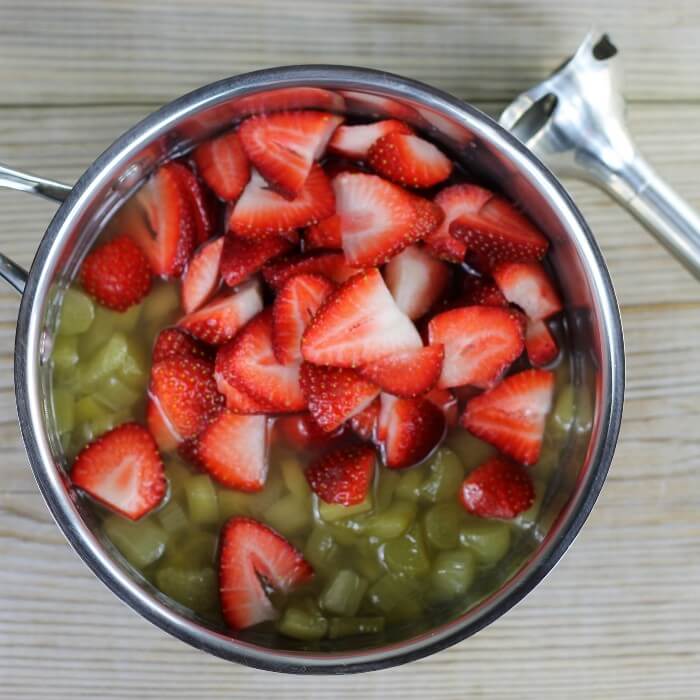 Looking down at a kettle with rhubarb and strawberries in it, with a immersible blender to the side.