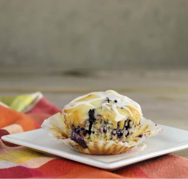 Blueberry muffin on a white plate with the paper cup pulled down.