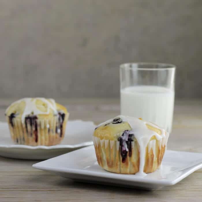 Sideview of a couple of muffins on white plates with a glass of milk.