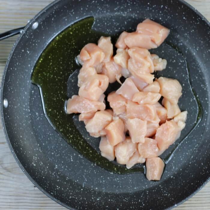 Small pieces of chicken and olive oil are added to a large skillet.