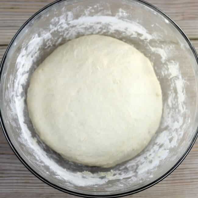Raised pizza dough in a glass mixing bowl.