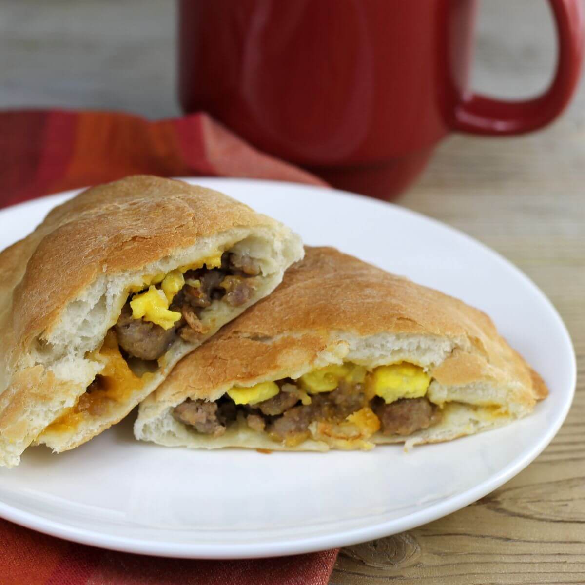 Side angle view of a breakfast cazone on a white plate with a red mug in back. 