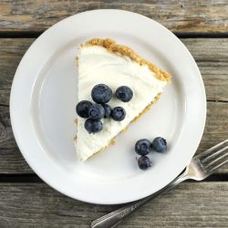 Lemon cream cheese pie topped with blueberries on a white setting on a wooden table.