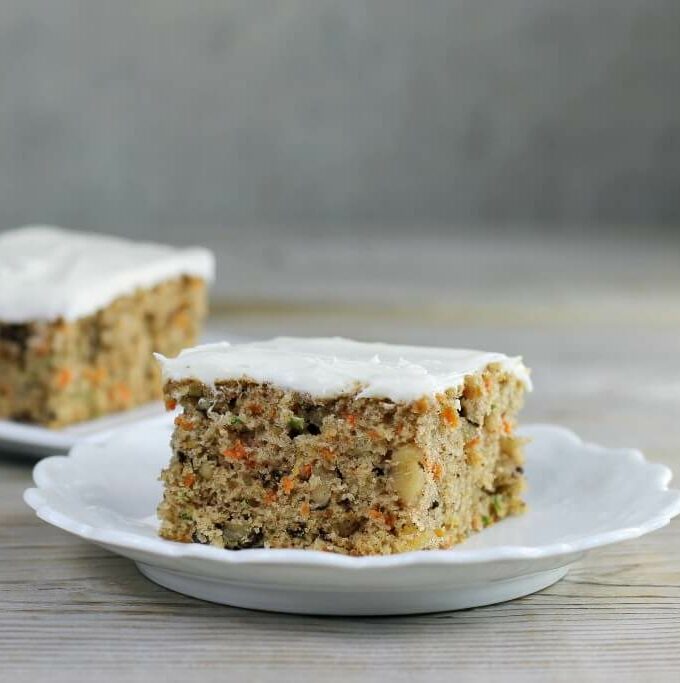 Looking at a side view of two pieces of carrot zucchini bars with cream cheese frosting.