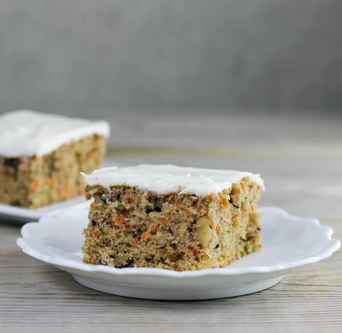 Looking at a side view of two slice of carrot zucchini bars with cream cheese frosting.