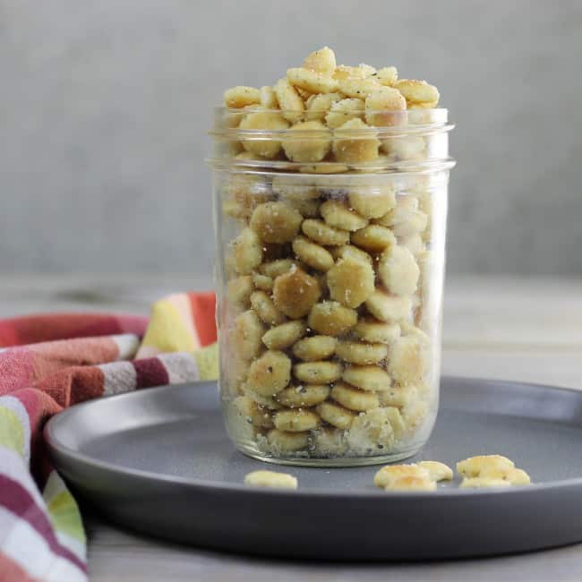Oyster crackers in a glass jar setting on a gray plate. 