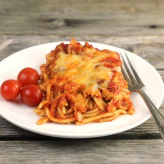 chicken spaghetti on a white plate with three cherry tomatoes on the side.