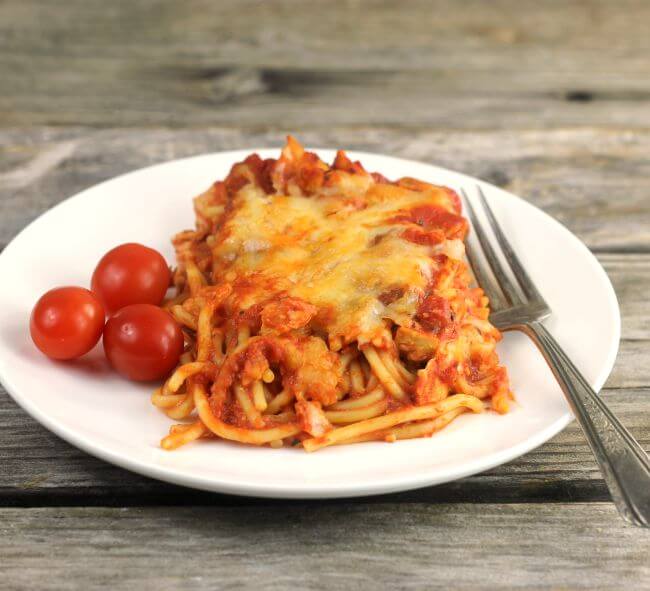 chicken spaghetti on a white plate with three cherry tomatoes on the side.