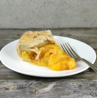 A slice of peach galette on a white plate with fork on side.
