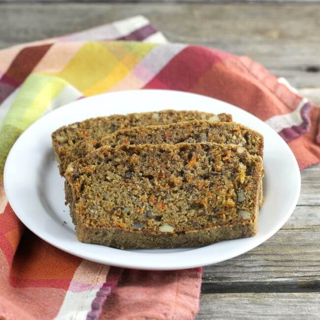 Slices of carrot quick bread on a white plate setting on a plaid napkin.