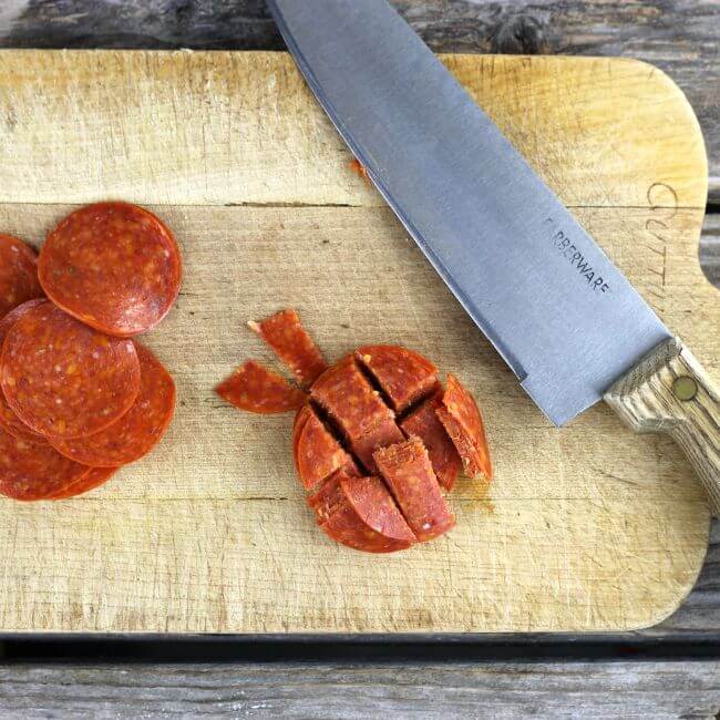 Wooden cutting board with pepperoni and knife.