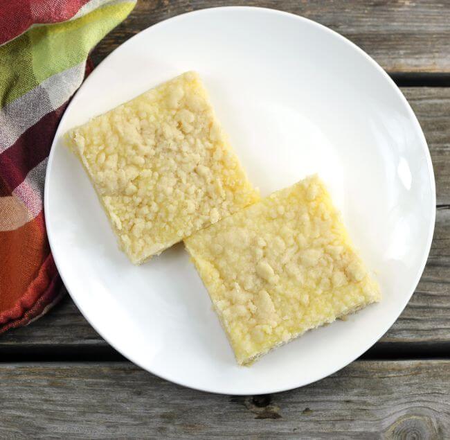 Two lemon bars setting on a white plate.