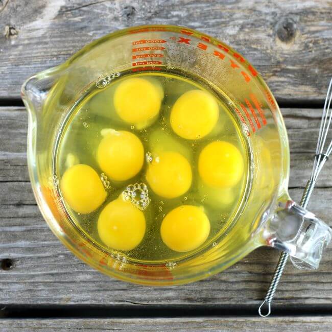 Raw eggs in a glass measuring cup with a small whisk