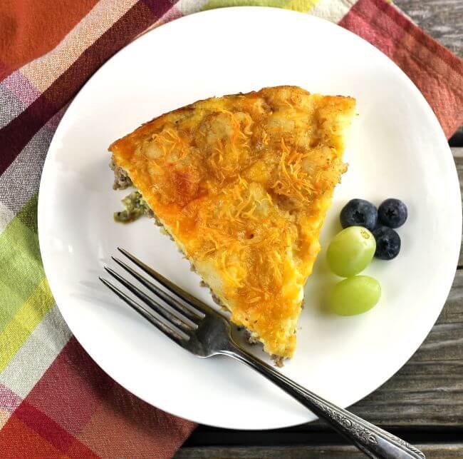Egg bake on white plate with grapes, blueberry, and fork on a plaid napkin