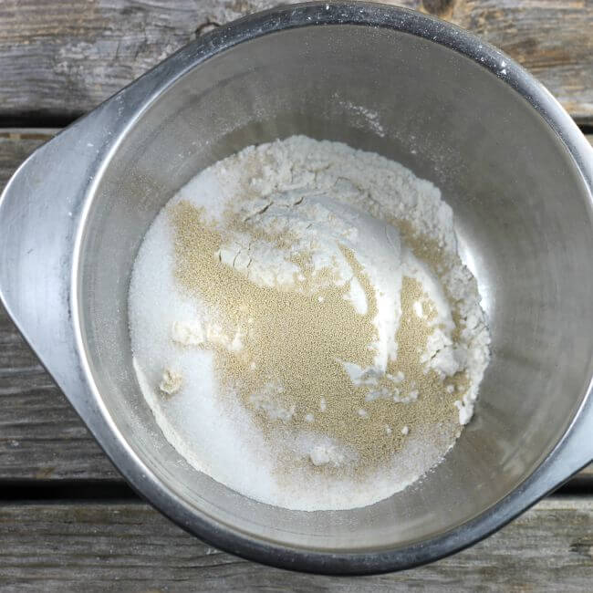 A stainless steel bowl with flour and yeast inside