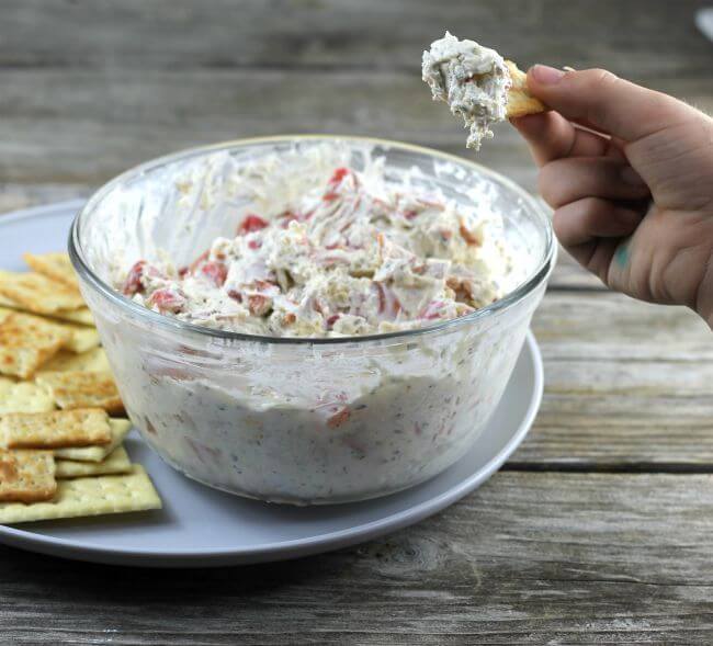 Pepperoni dip with hand holding a cracker with dip on it.