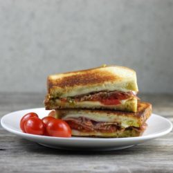 Pesto grilled cheese with salami with cherry tomatoes on a white plate.