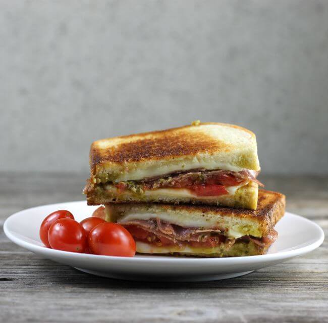 Pesto grilled cheese with salami with cherry tomatoes on a white plate.