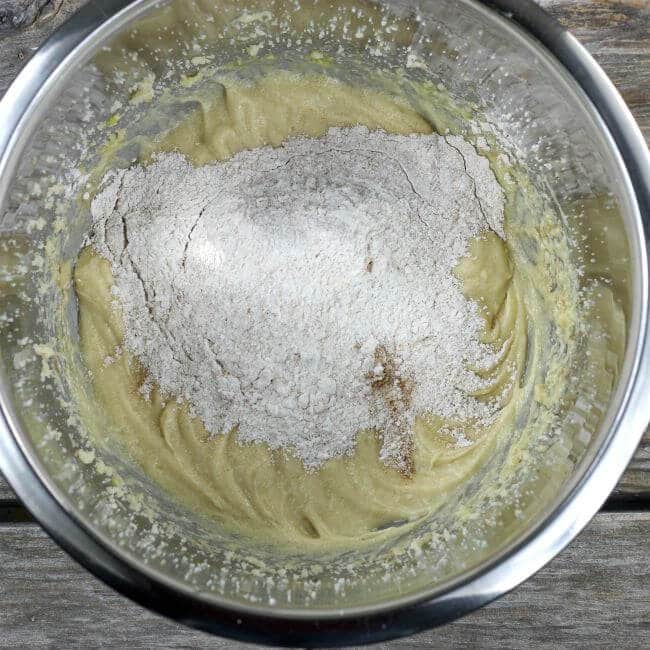 Adding flour to cake batter in stainless steel bowl.