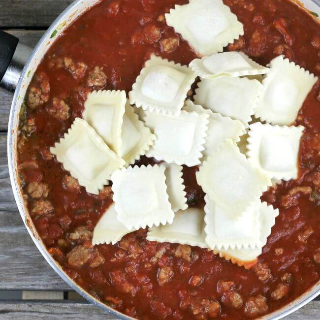 Frozen ravioli on top of Italian sausge and tomato sauce in a skillet.