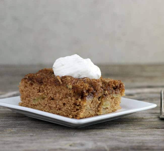 Apple cake topped with whipped cream on white plate.