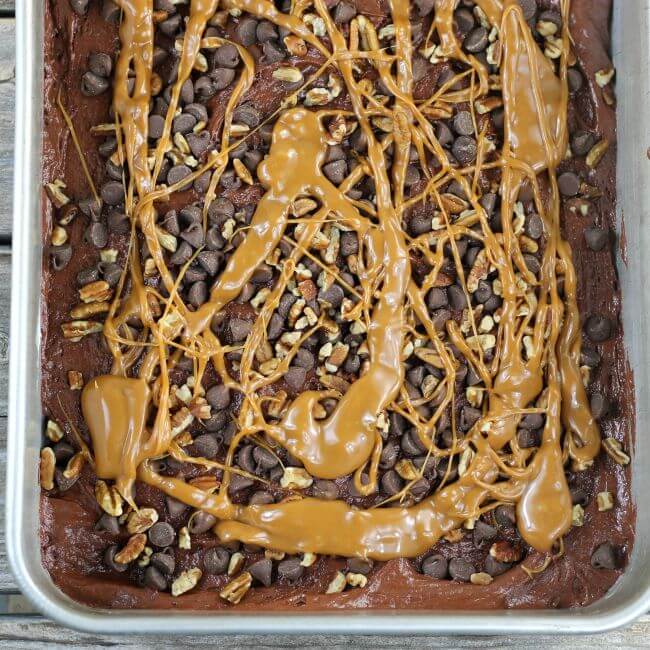 Turtle cake batter with chocolate chips, pecans, and caramel sauce in a baking pan.